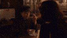 a woman is sitting at a table with a man holding a cup of coffee and says " tits up "