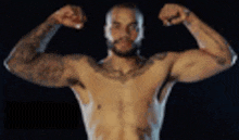 a shirtless man with a beard is flexing his muscles in a dark room .