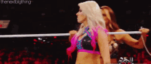 two female wrestlers are standing in a ring holding a rope .