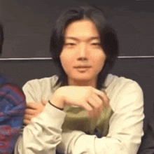 a young man with long black hair is sitting with his hands on his hips .