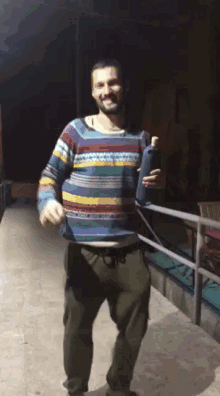 a man wearing a colorful sweater is holding a bottle