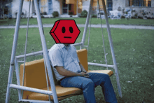 a man is sitting on a swing with a red cube on his head