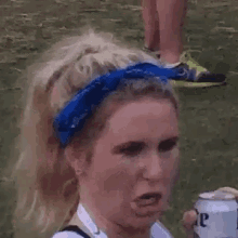 a woman wearing a blue bandana and a white shirt is holding a can of beer .