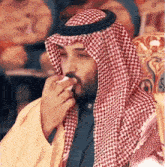 a man with a beard is wearing a red and white checkered head scarf and smoking a cigarette .