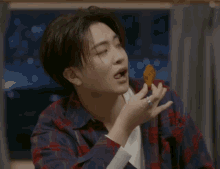 a young man in a plaid shirt is eating a piece of food with his finger in his mouth .