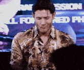 a man in a hawaiian shirt stands in front of a screen that says " all for red "