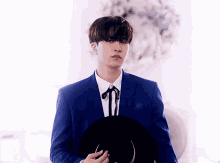 a young man in a blue suit and white shirt holds a black hat