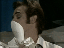 a man wearing a mask holds a newspaper in his mouth