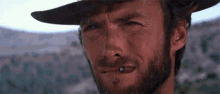 a close up of a man with a beard wearing a hat with a bullet in his mouth .