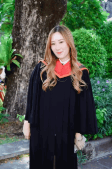 a woman in a graduation cap and gown stands in front of trees