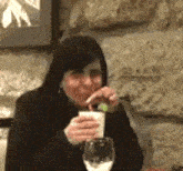 a woman is sitting at a table drinking from a cup while eating a grape .