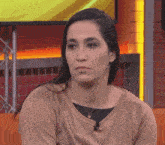 a woman wearing a gold sweater and a gold necklace looks to the side