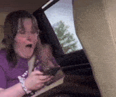 a woman in a purple shirt is sitting in the back seat of a car looking at her phone .