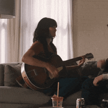 a woman playing a guitar while sitting on a couch