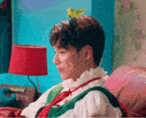 a man wearing a flower headband is sitting on a couch in front of a lamp .