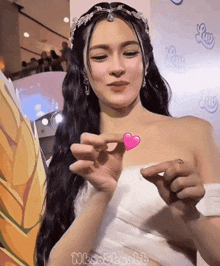 a woman in a white dress is holding a small pink heart in her hand