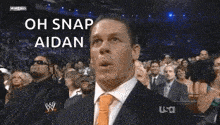 a man in a suit and tie is making a funny face while sitting in front of a crowd of people .