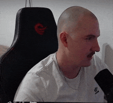 a bald man with a mustache is sitting in a chair with a microphone in front of him .