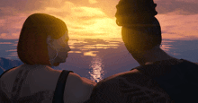 a man and a woman are looking at a sunset over a body of water