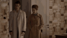 a man in a white coat stands next to a woman in a room