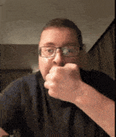 a man wearing glasses and a black shirt holds his fist up to his mouth