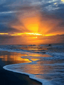 a sunset over a beach with waves crashing on the shore