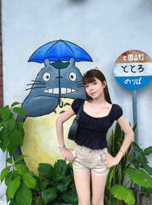 a girl stands in front of a painting of a totoro with an umbrella