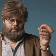 a man with a beard and glasses holds a sausage in his hand .