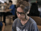 a woman wearing glasses and a t-shirt is sitting at a table looking down .