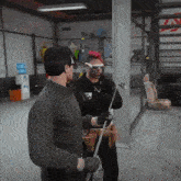 a man with a mohawk and sunglasses is talking to another man in a garage