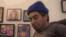 a man wearing a blue beanie is making a funny face in front of a wall of framed pictures