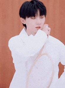 a young man with black hair is wearing a white shirt and holding his neck .