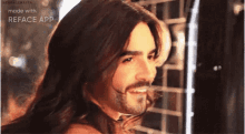 a man with long hair and a beard is smiling while standing in front of a mirror .
