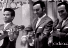 a black and white photo of three men playing guitars and tambourine