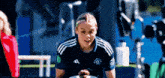 a woman in a blue adidas shirt is sitting on a soccer field .