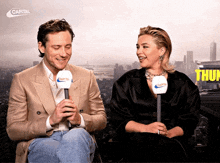 a man and a woman are sitting next to each other with microphones in front of a sign that says capital on it