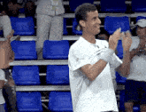 a man in a white shirt applauds in front of a row of blue seats