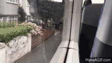 a train is going down a street with a brick wall and flowers in the background