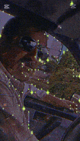 a man wearing sunglasses is driving a car with a reflection of trees in the windshield