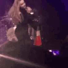 a woman is singing into a microphone while standing on a stage in front of a drum set .