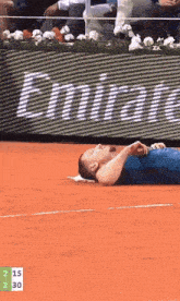a man is laying on a tennis court in front of an emirates sign