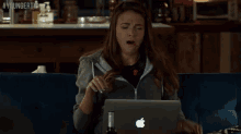 a woman sits on a couch with her eyes closed and an apple laptop in front of her