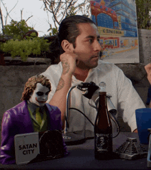 a man sitting at a table with a sign that says satan city on it