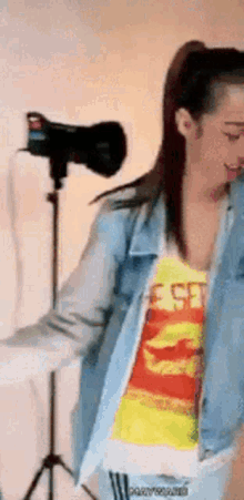 a woman in a denim jacket and a yellow shirt is dancing in front of a camera