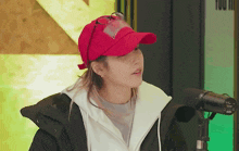 a woman wearing a red hat and a black jacket stands in front of a microphone