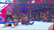 a referee is standing in the middle of a wrestling ring while two wrestlers are laying on the floor .