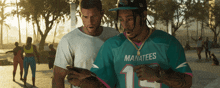 a man wearing a manatees jersey is looking at a cell phone