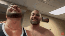 a shirtless man laughs with another shirtless man in a room with a sign that says ' nbc ' on it