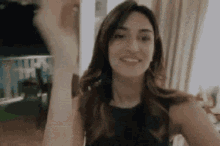 a woman in a black tank top is smiling and waving her hand .