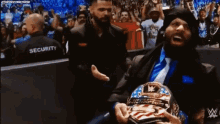 a man in a suit and tie is holding a wrestling championship while a security guard stands behind him .